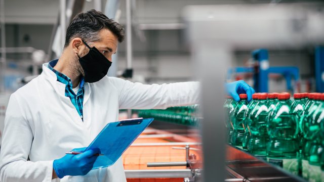 Male worker in workwear and with protective mask on his face wor Male worker in workwear and with protective mask on his face working in bottling factory. Inspection quality control.